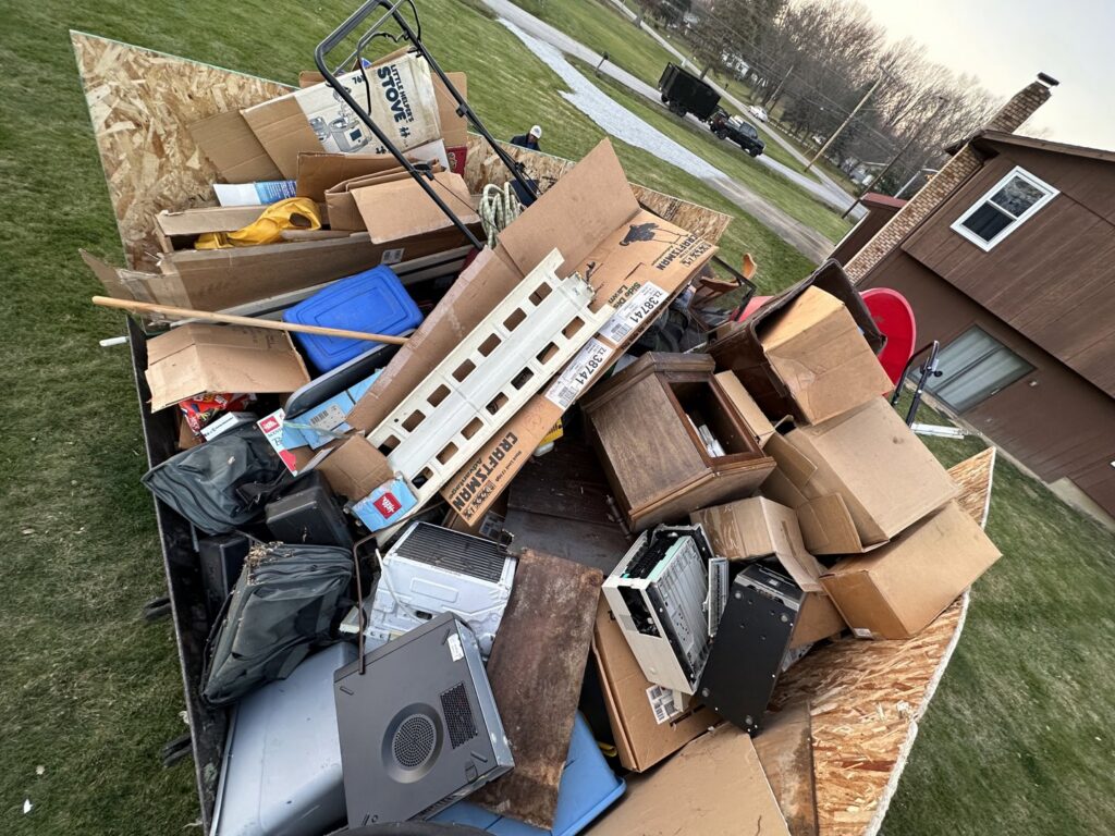 A dump trailer filled with various household junk, cardboard boxes, electronics, and a lawnmower for Sos Junk Removal in Akron, OH.