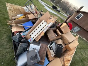 A dump trailer filled with various household junk, cardboard boxes, electronics, and a lawnmower for Sos Junk Removal in Akron, OH.
