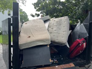 A dump trailer filled with old mattresses, furniture, and household junk by Getting Trashed Dumpster Rentals & Excavation in Assonet, MA.