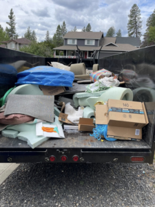 A dump trailer filled with various household junk, including foam, boxes, and furniture, for removal by Timber Moose Dynamics LLC in Spokane, WA.