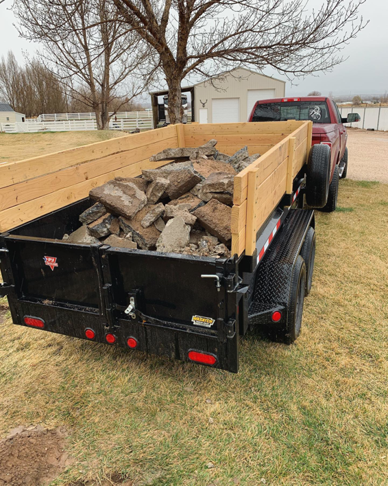 A red truck pulling a dump trailer filled with concrete debris for removal by S&J Rental and Removal in Ogden, UT.