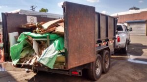 A dump trailer attached to a pickup truck, filled with cardboard, wood, and various debris, ready for removal by Lemcor in Newark, NJ.