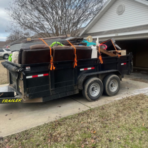 A black dump trailer filled with furniture and various junk items, ready for removal by Primo Operations in North Little Rock, AR.