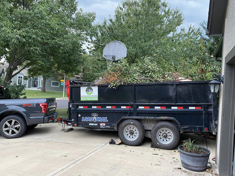 A dump trailer filled with branches and yard waste, attached to a pickup truck for D's Dumpster Rentals, Overland Park, KS.