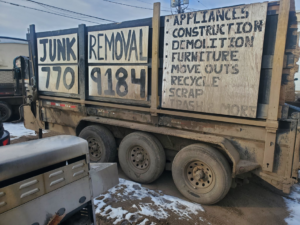 A large dump trailer with "JUNK REMOVAL" painted on the side, filled with items by 701 Scrap in Williston, ND.