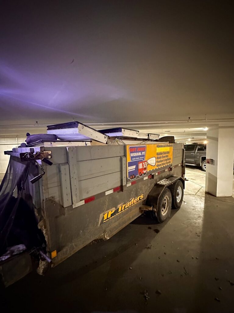 A WeHaul Hauling & Junk Removal dump trailer loaded with debris and large items, parked in a garage in Sioux Falls, SD.