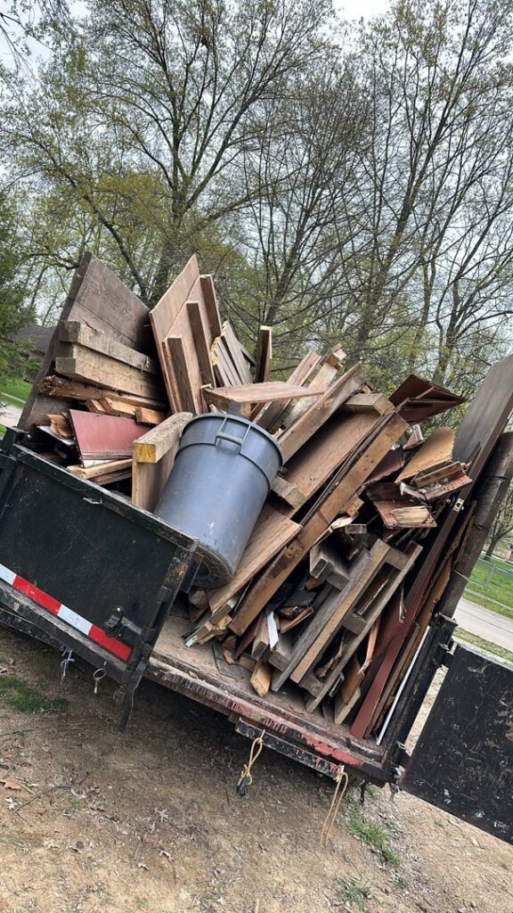 A dump trailer loaded with a large pile of wood scraps and a trash can, handled by Sos Junk Removal in Akron, OH.