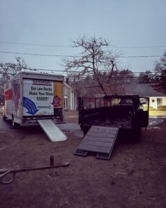 A dump trailer with its ramp lowered, parked next to a U-Haul truck by Getting Trashed Dumpster Rentals & Excavation in Assonet, MA.