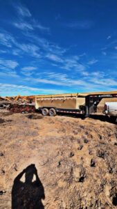 A Bin Suave LLC dump trailer and truck parked on a job site with debris piles in Espanola, NM.