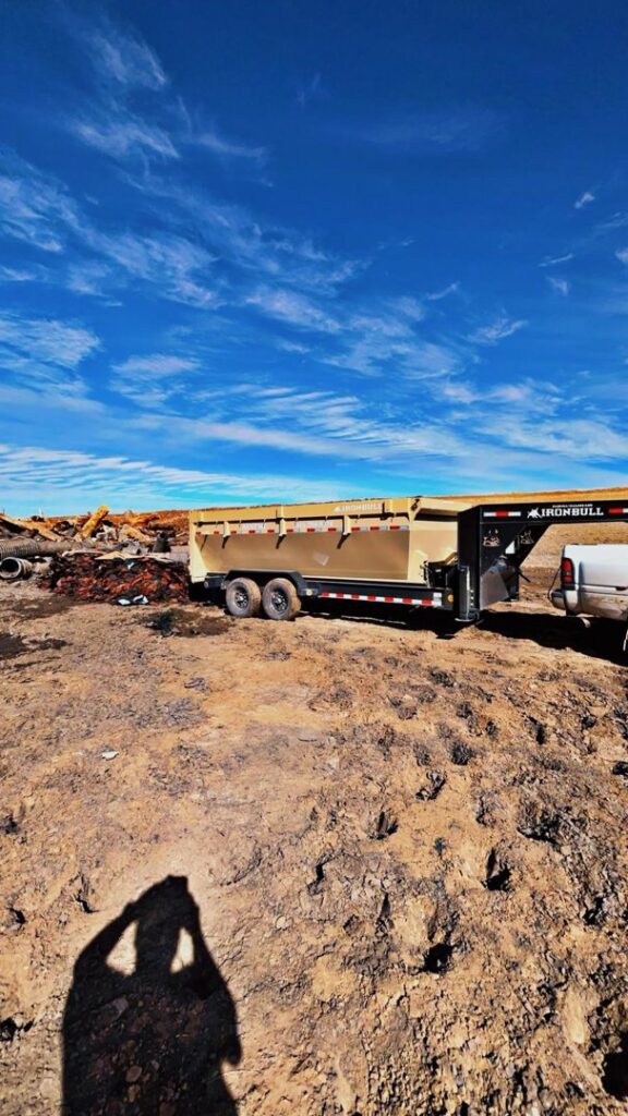 A Bin Suave LLC dump trailer and truck parked on a job site with debris piles in Espanola, NM.