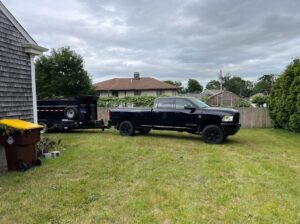 A black dump trailer parked on a residential lawn, ready for junk removal by Getting Trashed Dumpster Rentals & Excavation in Assonet, MA.