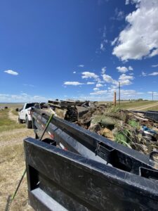A dump trailer overflowing with various junk and debris in a rural setting, handled by Hudson's Trash Removal, LLC in Great Falls, MT.
