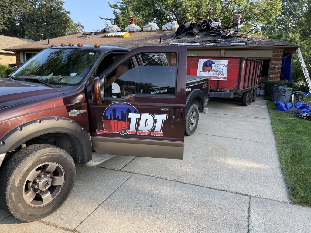 A The Dump Town truck and dump trailer at a roofing job site, providing junk removal services in Detroit, MI.