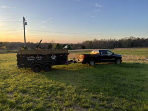 A dump trailer being towed by a pickup truck in a grassy field at sunset by Salt Creek Disposal in Bowling Green, KY.