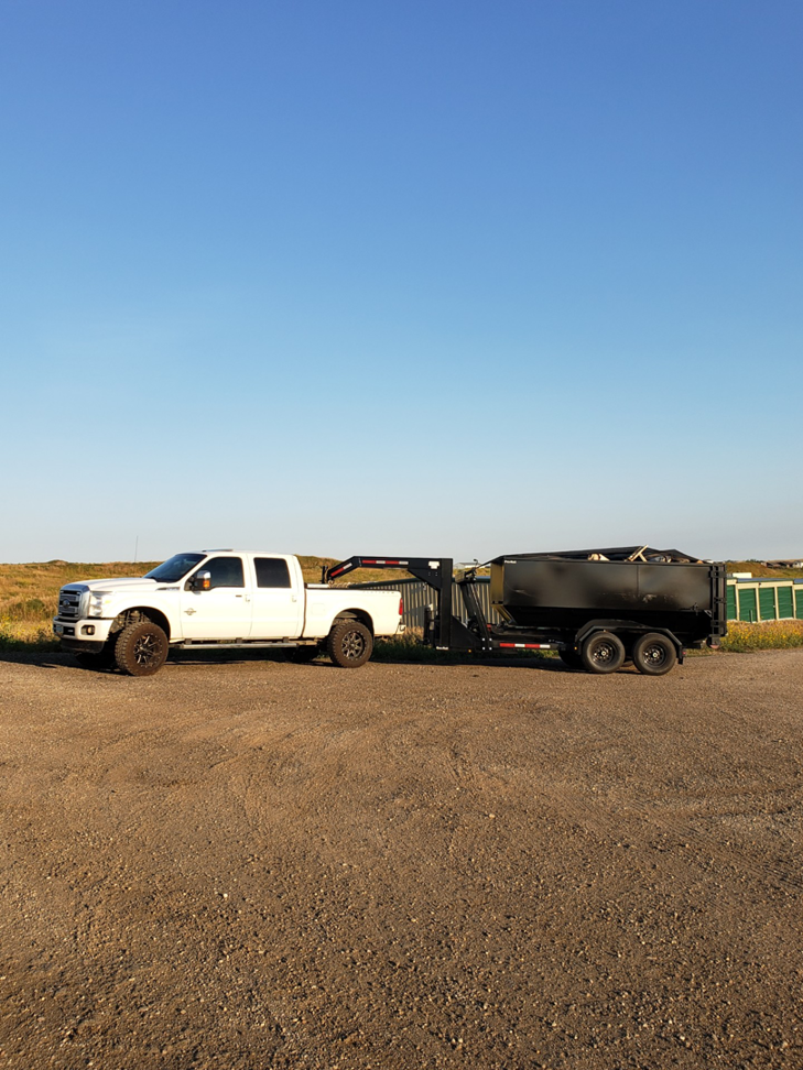 A white Ford truck with an empty dump trailer parked on a dirt lot, ready for junk removal services from Outlaw Rental in Bismarck, ND.