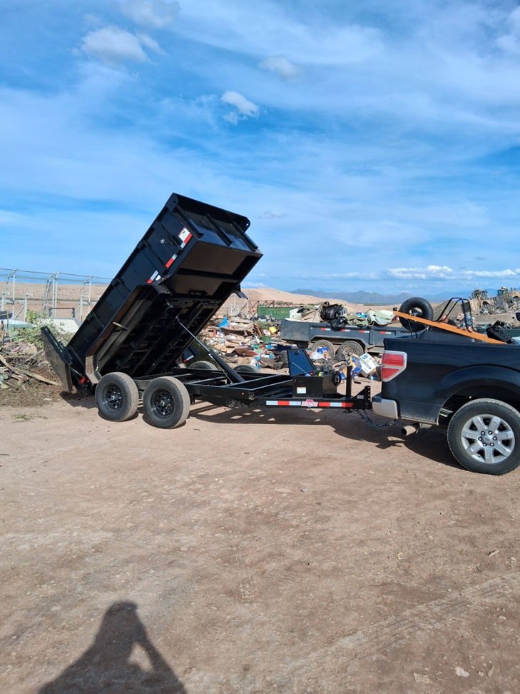 A black dump trailer attached to a pickup truck, tilted for unloading debris, by Arizona Best Junk Removal & Hauling in Tucson, AZ