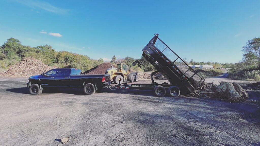 A black dump trailer unloading a large pile of debris at a yard by Getting Trashed Dumpster Rentals & Excavation in Assonet, MA.