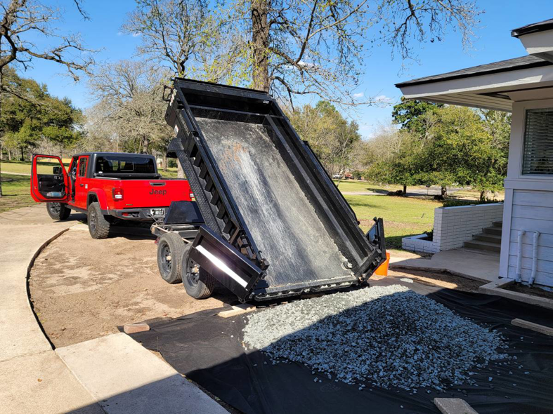 A dump trailer unloading gravel onto a prepared site next to a house, performed by Team512 in Austin, TX