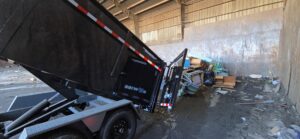 A black dump trailer with its bed raised, unloading junk and debris onto a pile inside a facility for Lemcor in Newark, NJ.