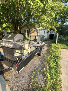 A dump trailer filled with a BBQ grill and other junk parked in front of a residential home, ready for removal by Speedy Scrap Junk Removal LLC in Portage, WI.