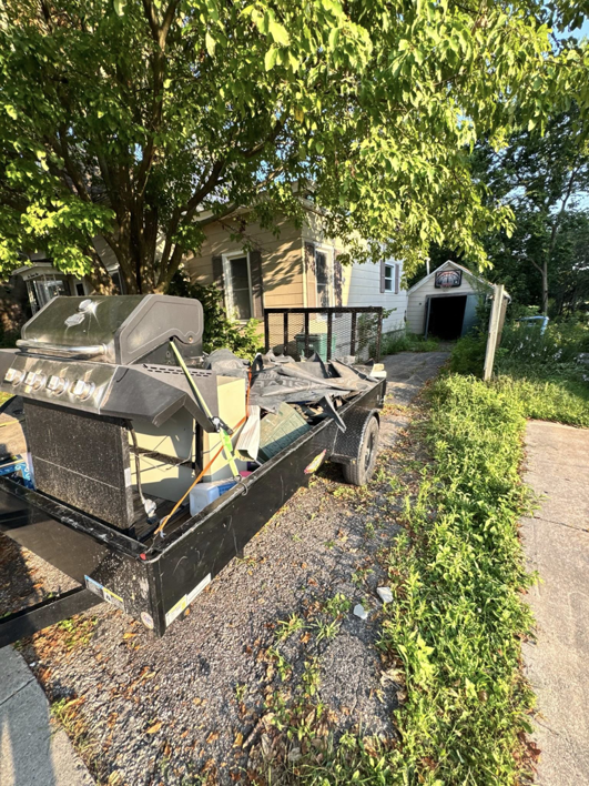 A dump trailer filled with a BBQ grill and other junk parked in front of a residential home, ready for removal by Speedy Scrap Junk Removal LLC in Portage, WI.