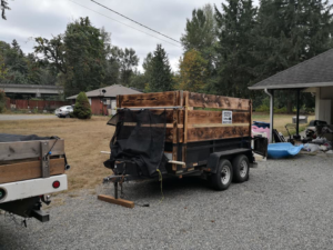 A dump trailer with wooden sides and a tarp, parked next to a pile of junk and debris, indicating a junk removal job by Gorilla Hauling in Kent, WA.