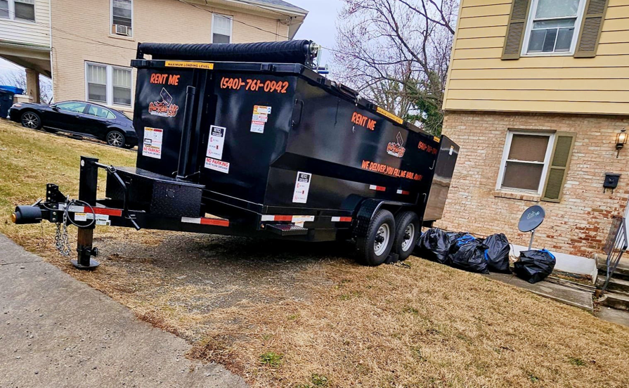 A black dump trailer parked in a driveway with trash bags, ready for junk removal by Haul Rollers LLC in Roanoke, VA.