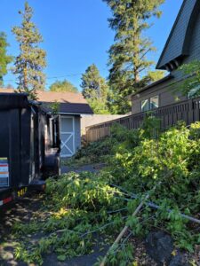 A dump trailer positioned next to a large pile of yard waste and tree trimmings for removal by Primetime Hauling and Junk Removal in Spokane, WA.