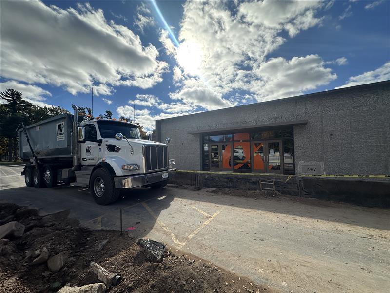 A white dump truck from Logistics Recycling Inc. parked at a construction site under a bright sky in Green Bay, WI.
