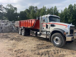 A Jr's Mini Roll Off LLC dump truck parked next to a large pile of construction debris in Byron, GA.