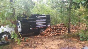 A Sharp Tree Service dump truck next to a pile of firewood, indicating tree removal and mulch services in Cumming, GA.