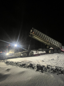A large dump truck with its bed raised, likely hauling wood chips or debris for Green Mtn Stump Grinding in Montpelier, VT.
