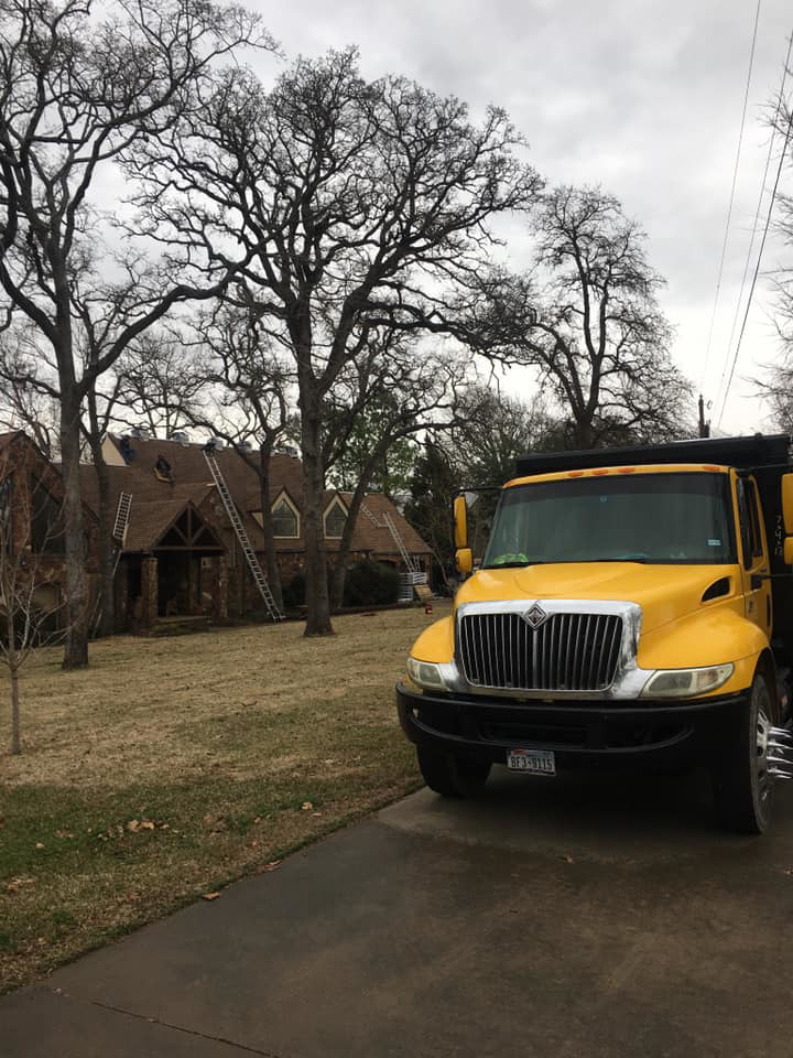 A yellow dump truck and ladders at a house roofing job site by TYCO Roofing & Construction LLC in Allen, TX.