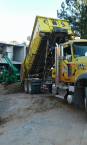 An Elite Waste Services dump truck unloading construction debris at a job site in Raleigh, NC.