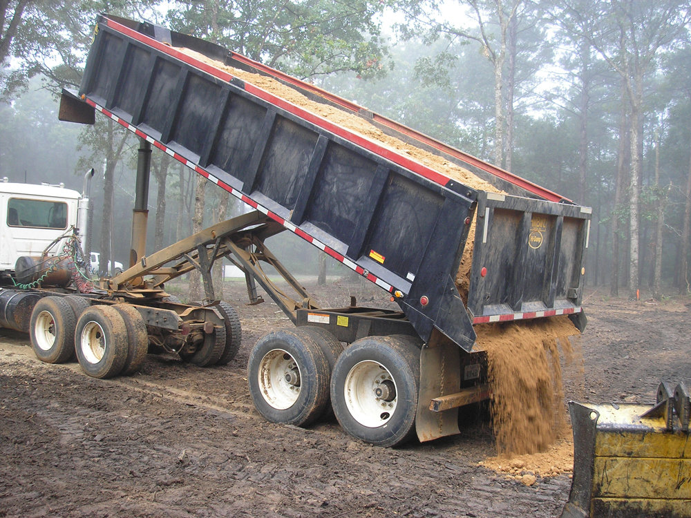 A dump truck unloading dirt or sand at a construction site by Daniel Dean Land Clearing & Dirt Work in Houston, TX.