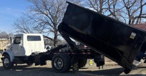A Wallburg Disposal Worx LLC dump truck tilting its black dumpster to unload junk in High Point, NC.