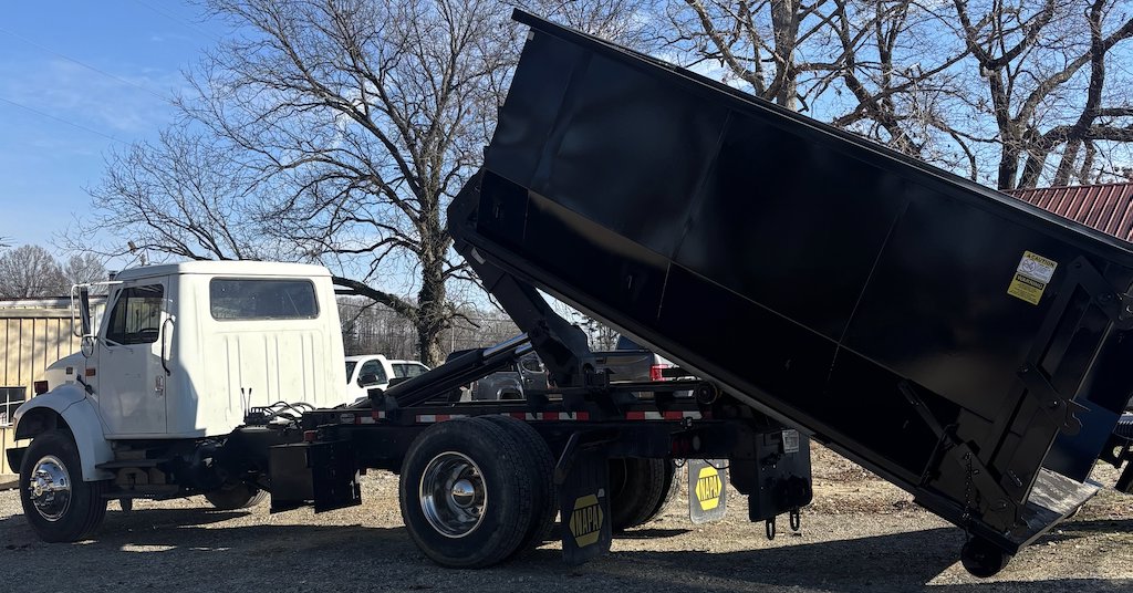 A Wallburg Disposal Worx LLC dump truck tilting its black dumpster to unload junk in High Point, NC.