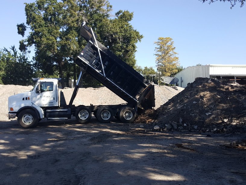 A dump truck unloading material onto a large pile at Global Recycling of Tampa Bay in Tampa, FL.