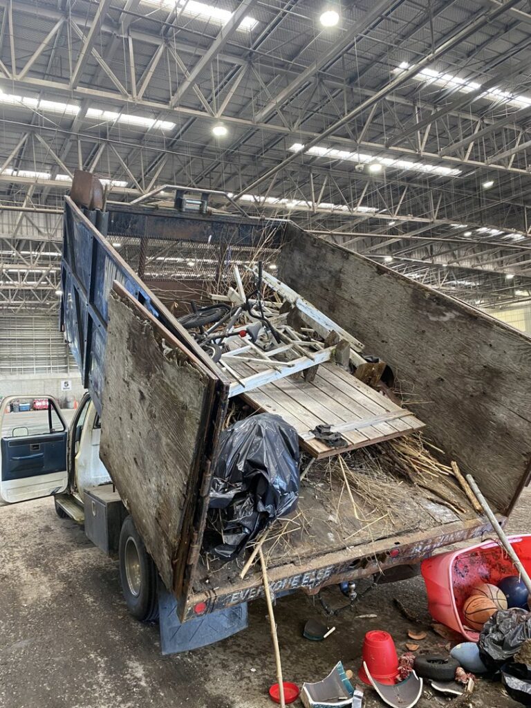 A dump truck with its bed raised, unloading a mixed load of junk and debris at a Down and Dirty Junk Removal site in Tacoma, WA.