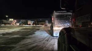 Several dump trucks lined up for snow removal services at night by Constantine Construction and Farm in Albany, NY.
