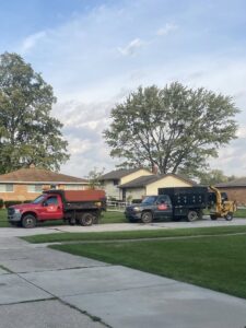 Two dump trucks and a wood chipper parked on a residential street, ready for a tree service job by Collier Lawn & Tree in Akron, OH.