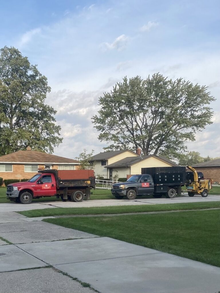 Two dump trucks and a wood chipper parked on a residential street, ready for a tree service job by Collier Lawn & Tree in Akron, OH.