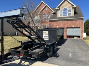 A Dumpin' Junk roll-off dumpster on a trailer in a residential driveway for junk removal in Martinsburg, WV.