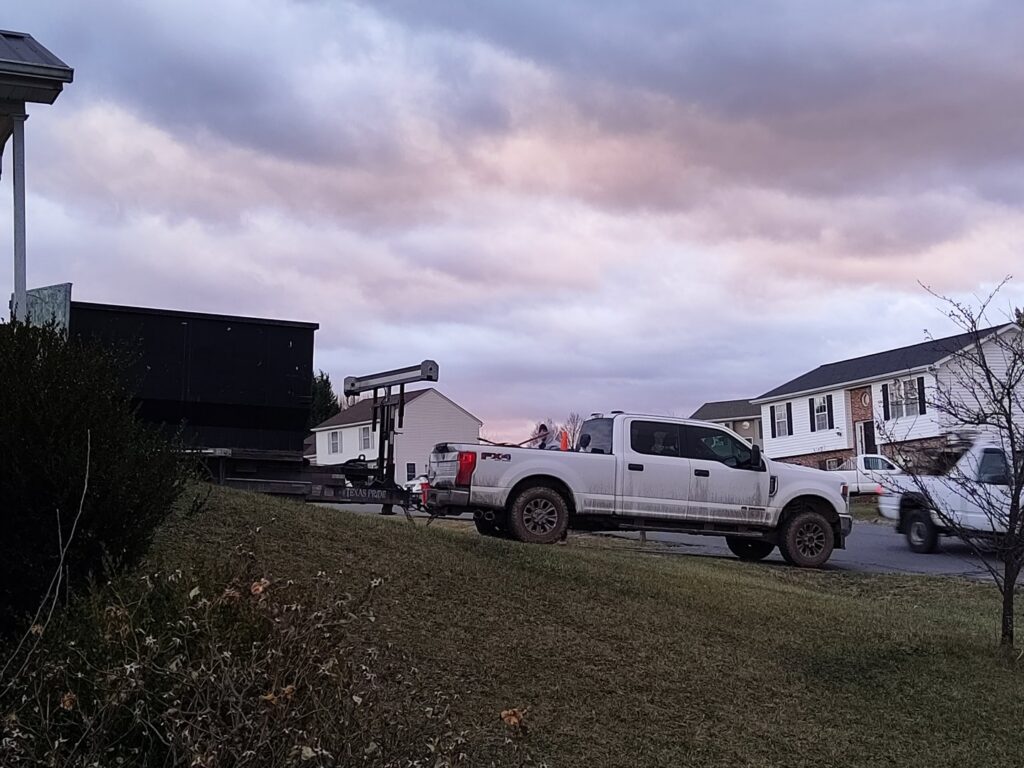 A Dumpin' Junk pickup truck towing a roll-off dumpster trailer in a residential neighborhood in Martinsburg, WV.