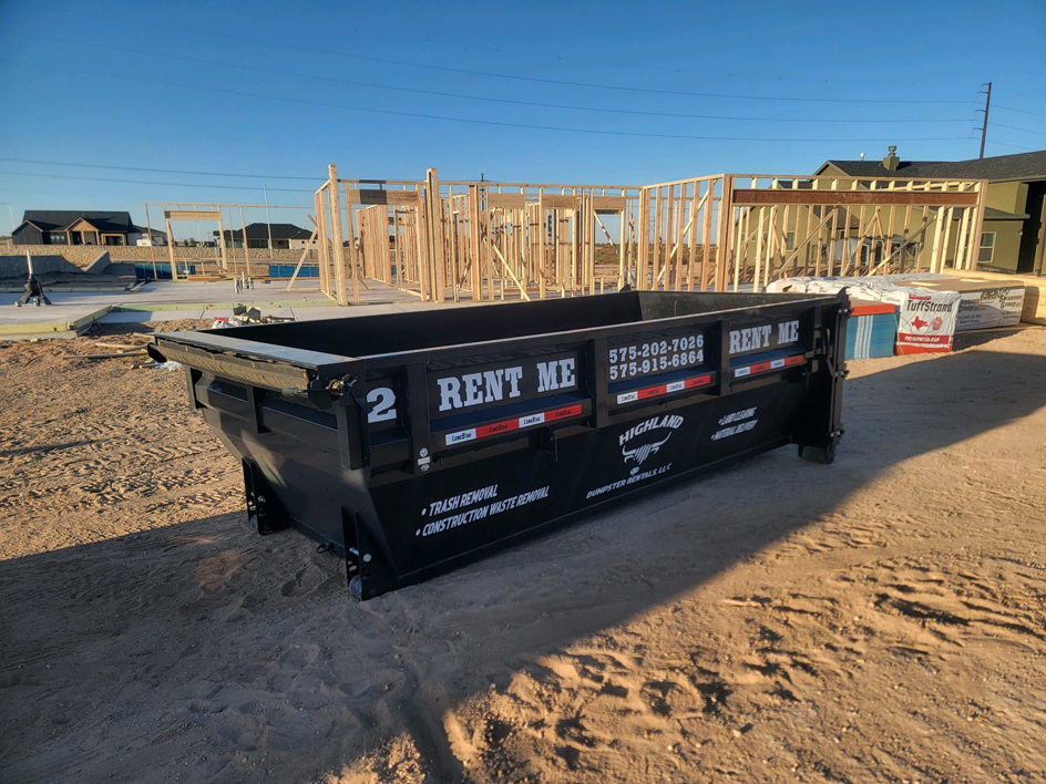 A black dumpster from Highland Dumpster Rentals LLC at a new construction site in Las Cruces, NM.