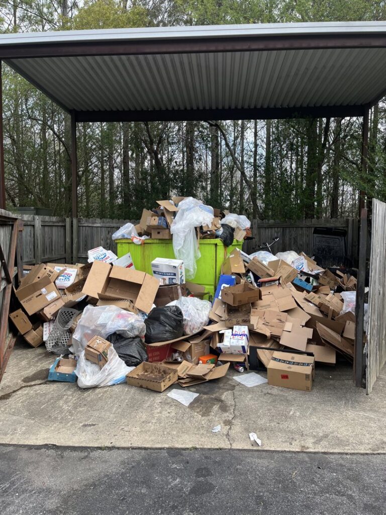 A dumpster area overflowing with cardboard boxes and trash bags, indicating a large junk removal job by LP Junk Removal in Birmingham, AL.