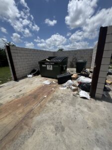A dumpster area with trash bags and debris on the ground, showing a junk removal site for Junk Out Boyz LLC in Georgetown, TX.