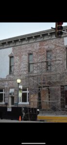 An MWT Dumpster and Hauling Services dumpster positioned next to a building with scaffolding for renovation debris removal in Morris, IL.