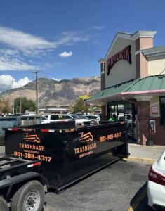 A TrashDash dumpster on a trailer parked outside a Maverik convenience store for commercial junk removal in West Haven, UT.