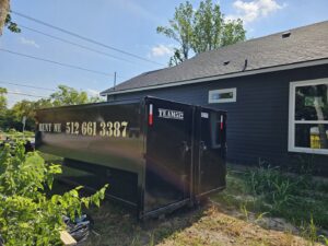A black roll-off dumpster from Team512 parked next to a newly sided house at a construction site in Austin, TX